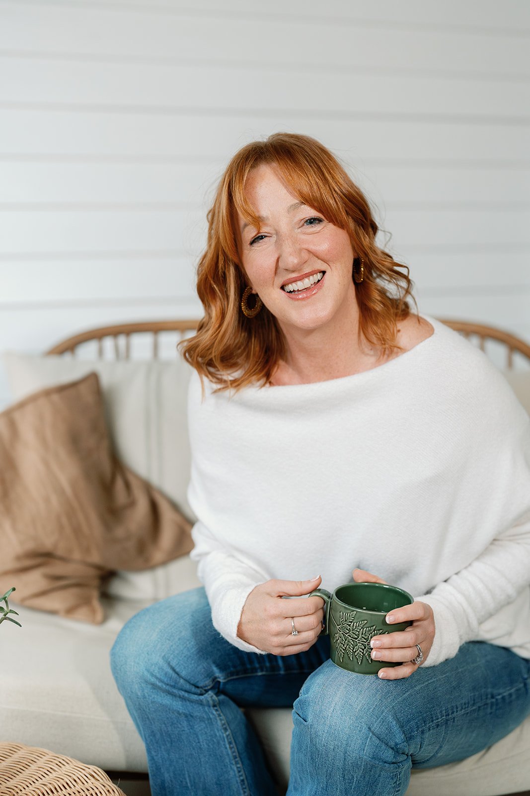 Amanda Alexander smiling, holding a green mug, wearing a cream jumper