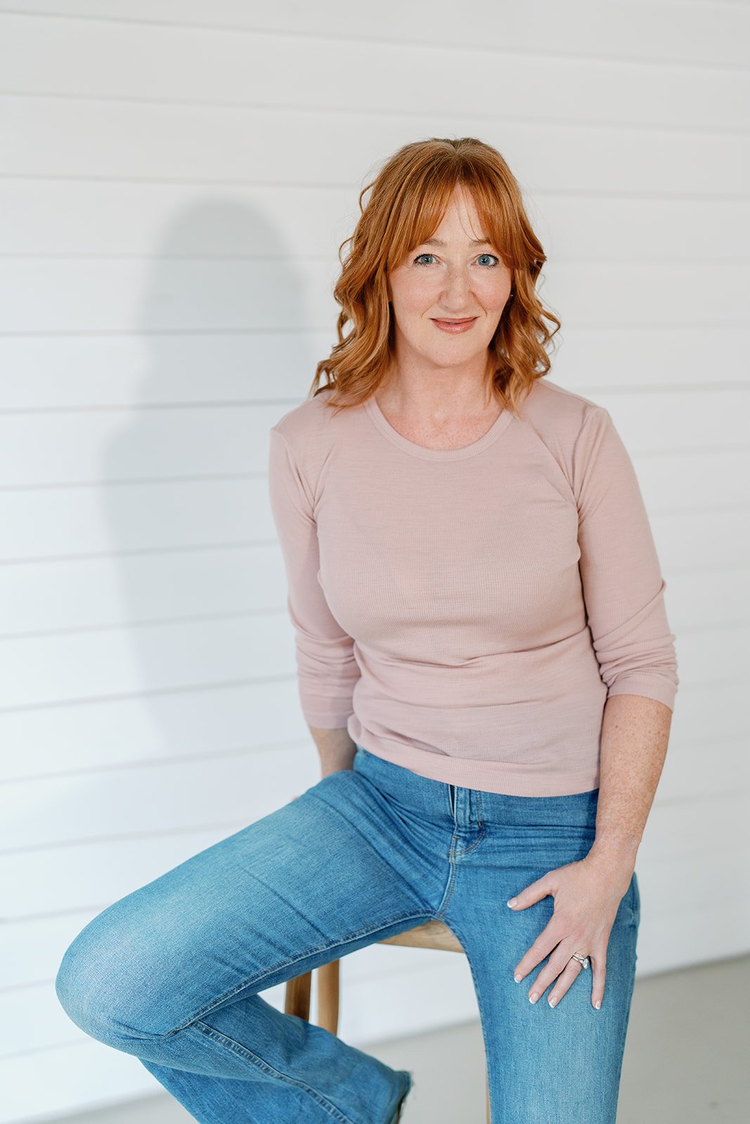 Amanda Alexander // Simply Headshots Amanda Alexander smiling, sat on a stool in a blush pink jumper and jeans